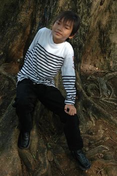 little asian boy sit down beside the tree in park