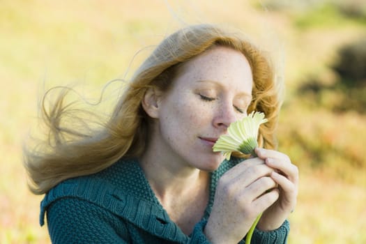 Portrait of a Pretty Redhead Woman Smelling a Flower