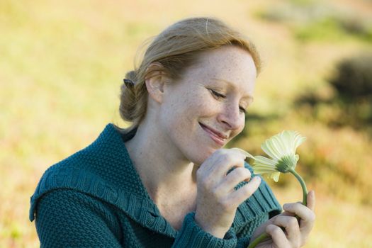 Portrait of a Pretty Redhead Woman Looking at a Flower