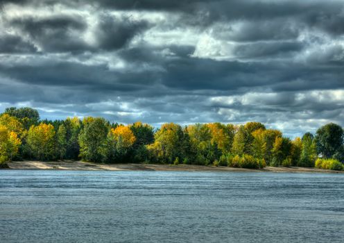 Autumn forest, river and dramatic sky. HDR image.