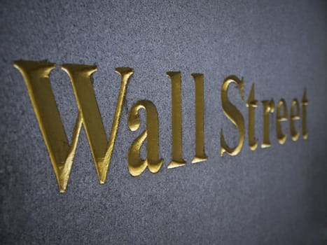 Wall Street carved in stone with golden letters.