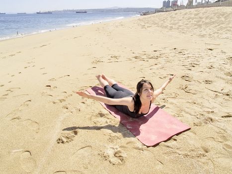 Yoga teacher practising at the beach pose paorna salabhasana