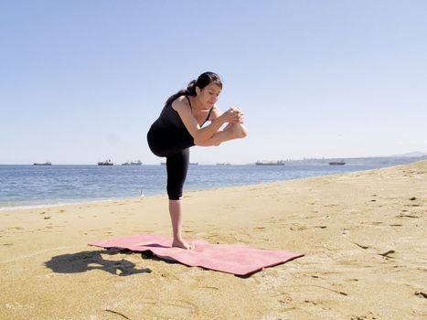 Yoga teacher practising at the beach pose dandayamana janushirasana