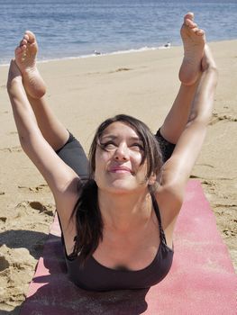 Yoga teacher practising at the beach pose dhanurasana