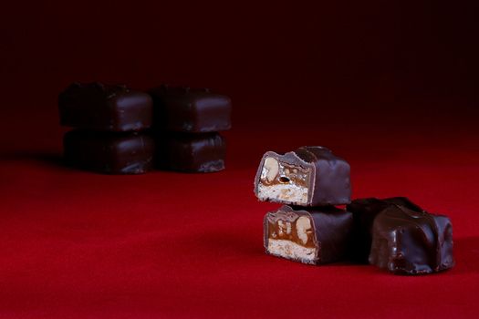 The chocolate with nuts is cut half-and-half. A red background, on a back background some chocolates.