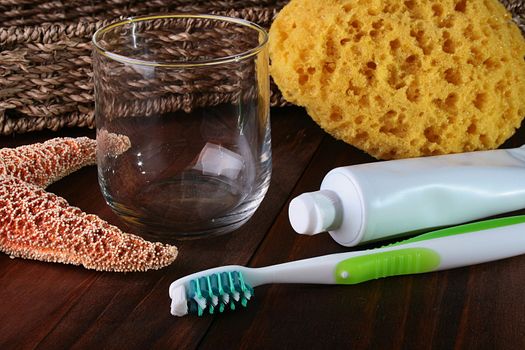 Set for hygiene: tooth paste and a brush, a bast and an empty glass glass. As a decor the basket and a starfish is added.