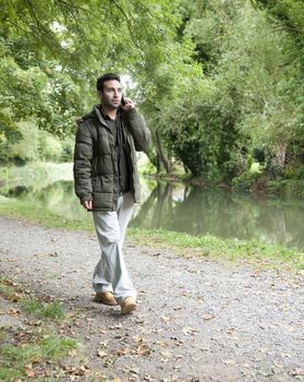 man on a mobile phone walking beside a canal or river