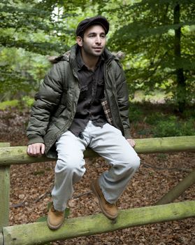 Man sitting on a fence in woodland.