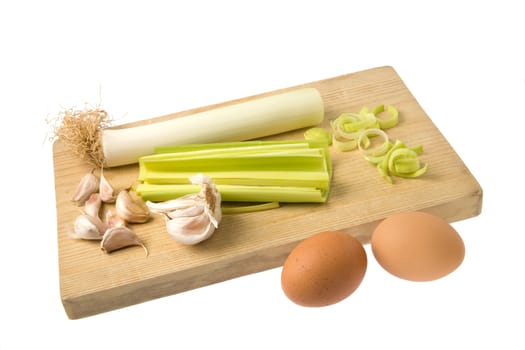 Group of eggs, leek and garlic on a wooden chopping board isolated against a white background.