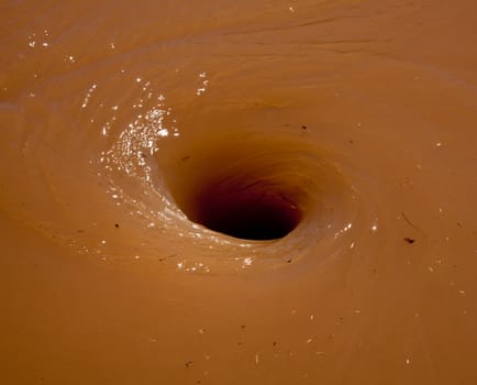 Deep brown flood water in river swirling into a whirlpool