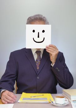 A businessman sits at his desk, holding a home-made smiley mask in front of his face. Look ... I'm happy ... really!