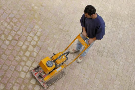 A builder using a machine to pack down bricks in a newly-paved courtyard.