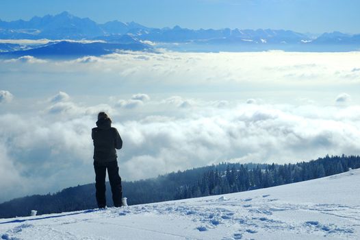 A skier, high on a slope in the Swiss Jura mountains in winter, takes a break from skiing and gazes across to the French Alps. The valley below is filled with cloud, what the Swiss call the 'Mer de Brouillard' (sea of mist).