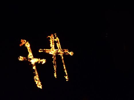Burning crosses being used as part of ritual, on black background