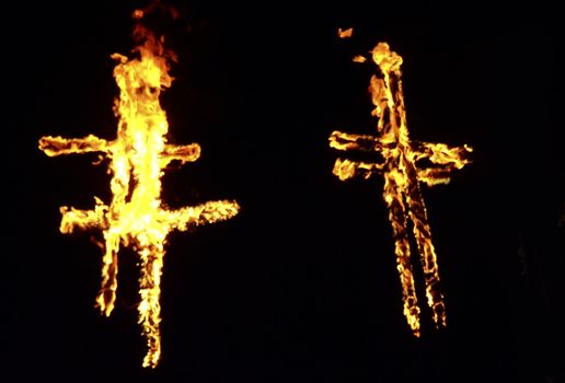 Burning crosses being used as part of ritual, on black background