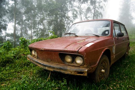 Brown old car abandoned in rural landscape with mist.