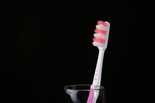 New red with white a tooth-brush in a glass on a black background.