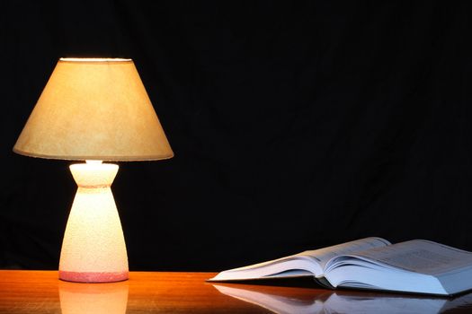 Vintage table lamp with shade near open book on dark background
