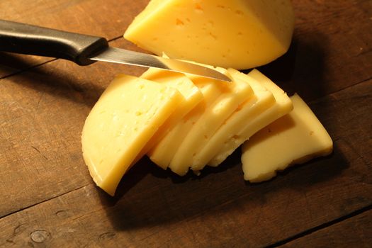 Sliced cheese and knife lying on wooden background