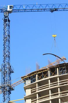 Crane and concrete building under construction on background with blue sky