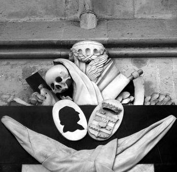 Memento mori (Remember thou shalt die) - Ancient medieval sculpture with skull and reaper's sickle in Koelner Dom cathedral, Koeln, Germany