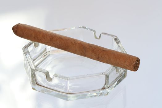 Glass ash-tray with cuban cigar isolated on gray background