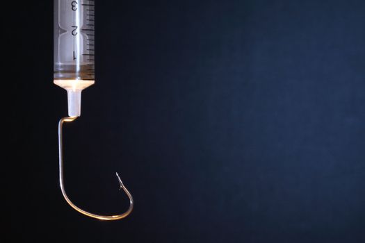 Closeup of syringe with fish hook as surgical needle on dark background