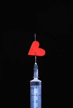 Plastic syringe with red paper heart on the needle isolated on black background