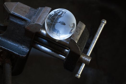 Glass globe inside old vise grip on dark background