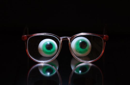Funny composition with two big toy eyes and spectacles isolated on dark background