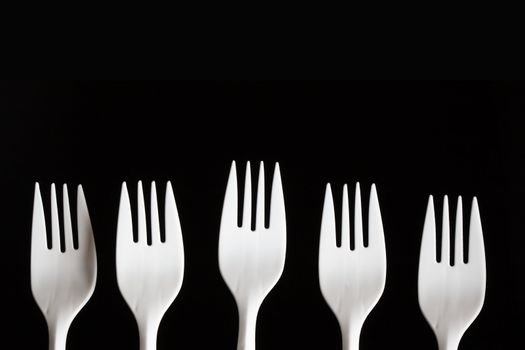 Five white plastic forks in a row shot on a black background