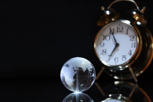 Glass globe and alarm clock on dark background with copy space
