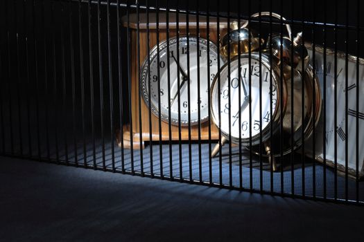 Three alarm clocks behind bars on dark background with copy space