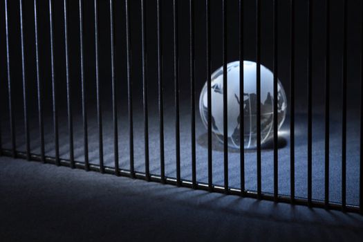 Glass globe behind bars on dark background with copy space