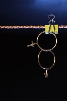 Crossing sex symbols made from brass wire hanging on dark background with rope