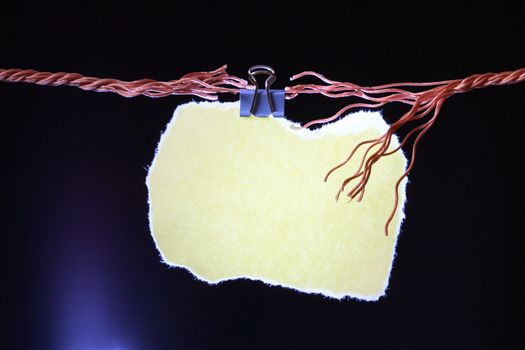 Blank yellow paper sheet for your notes hanging on dark background with rope