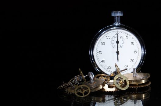 Gearwheels near standing stopwatch on dark background with copy space