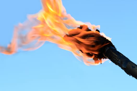 Closeup of flaming torch on blue background with copy space