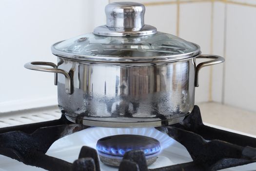 Metal cooking pot standing on kitchen stove with flame. Image with clipping path for using another backgrounds