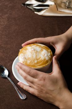 Closeup of female hands holding cup of Cappuccino