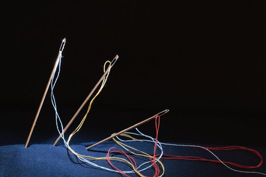Closeup of three sewing needles standing on black background