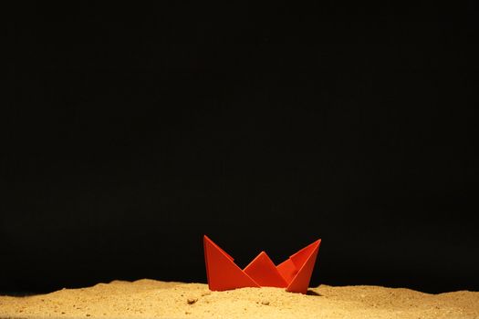 Red paper boat in sand on black background