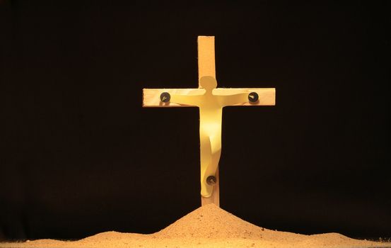 Paper man hanging on wooden cross woth thumbtacks on black background