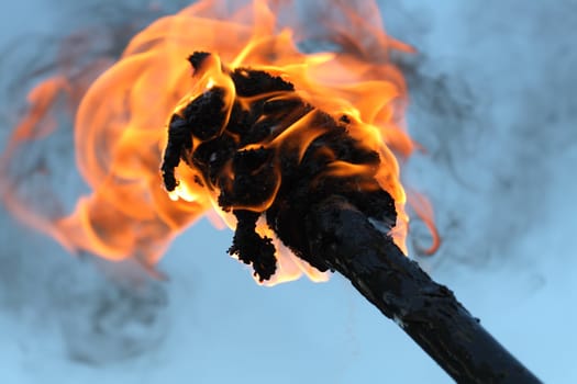 Closeup of flaming torch with fire and black smoke on blue background