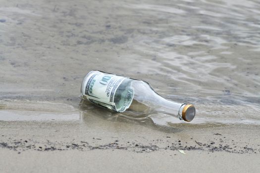 One hundred dollars note inside glass bottle lying in water on the river bank