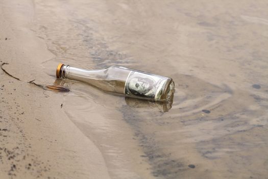 One hundred dollars note inside glass bottle lying in water on the river bank