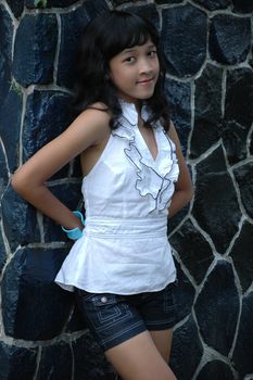 little asian girl stand up beside rock wall in park
