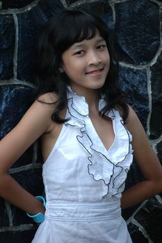 little asian girl stand up beside rock wall in park
