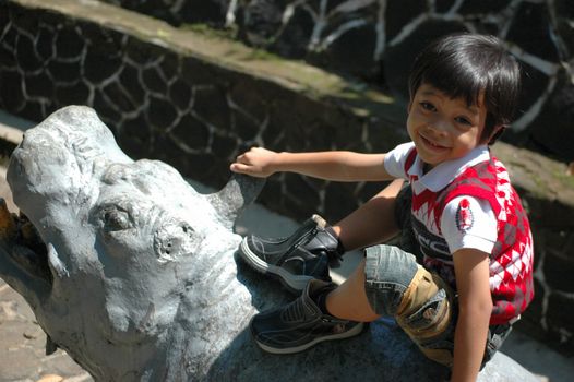 little asian boy sit down on zeebra statue in park
