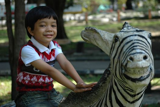 little asian boy sit down on zeebra statue in park
